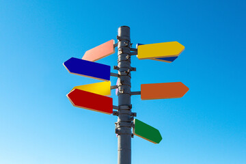 Signpost with bright colored arrows against blue sky