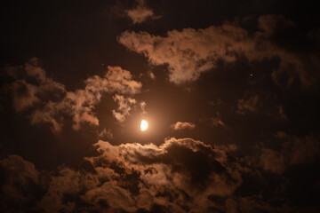 first quarter moon on the night sky seen trough brightly clouds during summer season