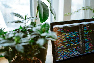 Html code on the laptop screen standing on a wooden table with home green plants, cozy working office. Selective focus