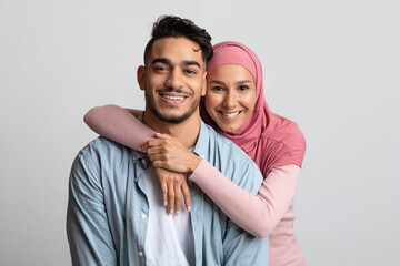 Fototapeta premium Portrait Of Muslim Couple Embracing Over Grey Background And Smiling At Camera