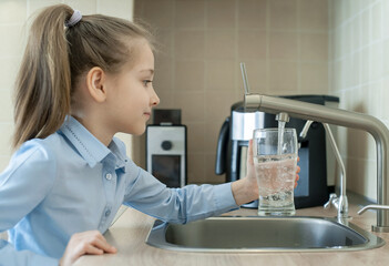 Little girl open a water tap with her hand holding a transparent glass. Kitchen faucet. Filling cup beverage. Pouring fresh drink. Hydration. Healthcare. Healthy lifestyle. World Water Day