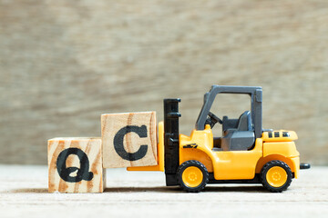 Toy forklift hold letter block C to complete word QC (Abbreviation of Quality Control) on wood background