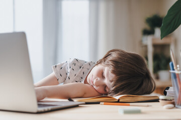 Distance learning online education. Caucasian smile kid boy studying at home, tired sleep and lying on laptop and doing school homework. Thinking child siting at table with notebook. Back to school.