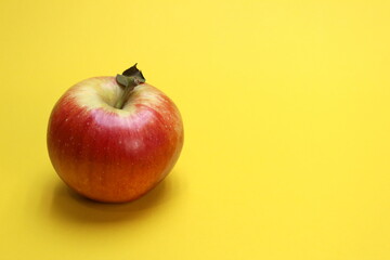 red apple with dry petal lies on yellow background