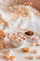 Ceramic cup of hot chocolate or cocoa with marshmallow on white table. Winter dessert beverage. Decoration garlands of lights