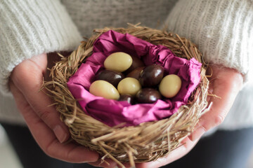 Woman hands holding a nest with sweet chocolate eggs