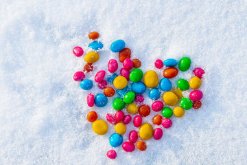 Multi-colored heart shaped candies in the snow. Sweets in the snow. Valentine's Day. Sweets as a gift. Romantic background for Valentine's Day.