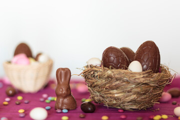 Bird nest with chocolate eggs and chocolate bunny and other easter sweets on table