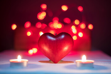 Red love heart illuminated by two candles with red and yellow light bubbles in the background