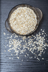 Dry oatmeal porridge in a transparent bowl on a dark background close-up, top view. Vertical photo