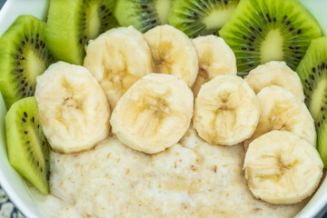 Oatmeal porridge with bananas, kiwi in a bowl on a dark background close-up. Healthy breakfast.