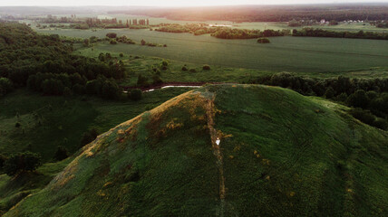 Young beautiful woman in boho style dress and hat on nature at sunset. Photo from a drone of a girl on the hills.