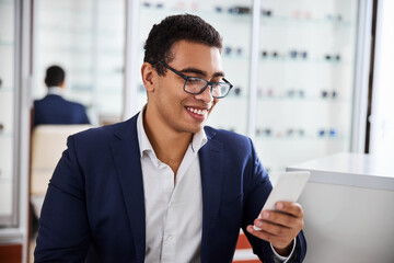 Man in eyelasses using his gadget in an optical store