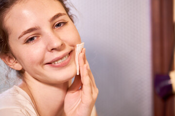 Portrait of young beautiful teenage girl wiping clean face with matifying toner or micellar water