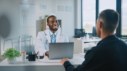 Family Doctor is Delivering Great News About Male Patient's Medical Results During Consultation in a Health Clinic. Physician in White Lab Coat Sitting Behind a Computer in Hospital Office. 