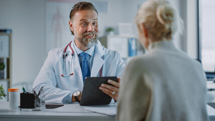 Friendly and Cheerful Family Doctor is Reading Medical History of Senior Female Patient During Consultation in a Health Clinic. Physician Using Tablet Computer in Hospital Office.