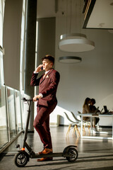 Young businessman standing by the office window with electric scooter © BGStock72