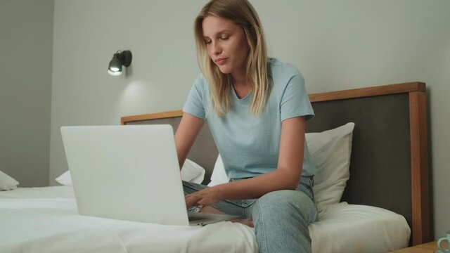 A smiling woman is using her laptop computer sitting in the bedroom
