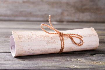 Diploma scroll close-up. Rolled paper with tie on wooden table.