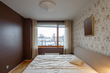 Contemporary interior of bedroom in modern flat. Cozy bed. Lamps on nightstands. Huge window. Hardwood floor.