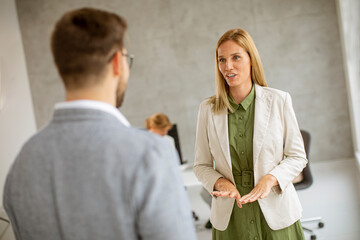 Man and woman business couple discussing indoors in the office with young people works behind them