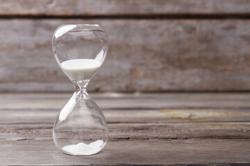 Hourglass with white sand close up. Grey wood background.