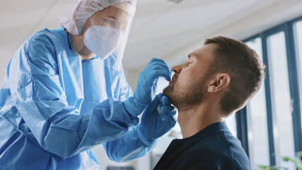 Medical Nurse in Safety Gloves and Mask, Protective Face Shield and Overalls is Taking a PCR Corona...