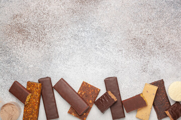Whey protein powder in measuring scoop and different energy protein bar on grey background. Top view