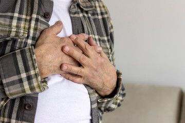 Photo of a senior male with chest pain. Elderly man suffering from heartburn or chest discomfort symptoms. Men having a pain in the heart area. Old man with eyeglasses having heart attack at home.