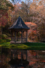 Gazebo in the garden in autumn with beautiful reflections of the fall trees vibrant colors in the water