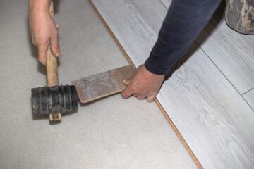 Craftsman installs light wood laminate tiles in the living area using a rubber mallet. Home and office renovation and improvement