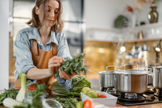 Pretty Woman With Green Ingredients And Spicy Herbs Cooking Healthy Food On The Kitchen. Healthy And Wellness Concept. High Quality Photo