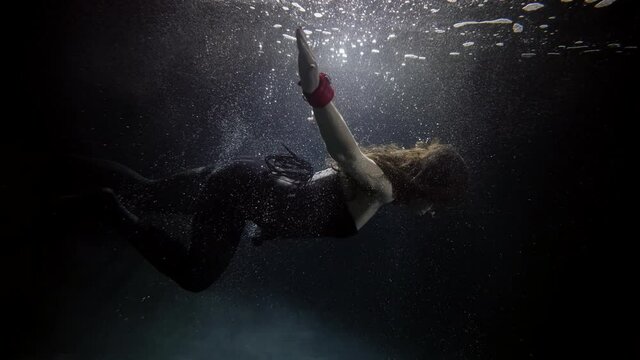 slim woman is floating underwater in darkness and depth, subaquatic shot