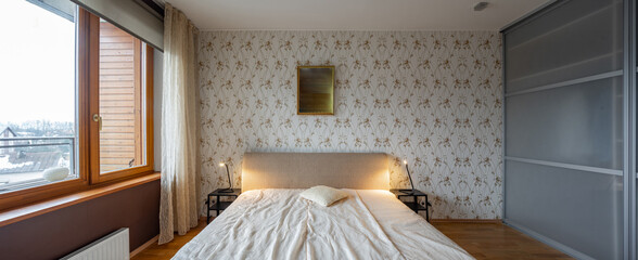 Contemporary interior of bedroom in luxury flat. Cozy bed. Nightstands. Huge sliding door wardrobe. Panorama view.