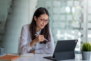 Beautiful Asian woman using tablet and notebook at her desk in the office.