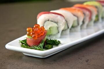 Assortment of Japanese sushi rolls nigiri, sashimi, maki, salmon, tuna and avocado served in long rectangular plate over stone background