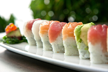Assortment of Japanese sushi rolls nigiri, sashimi, maki, salmon, tuna and avocado served in long rectangular plate over stone background, close up view