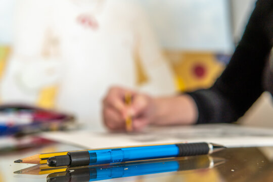 Close-up of a blue pen on a glass table, in the background out of focus the hands of an illustrator making a drawing in an artist's studio