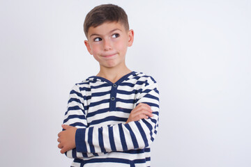 little cute boy kid wearing red stripped t-shirt against white wall bitting his mouth and looking worried and scared crossing arms, worry and doubt.
