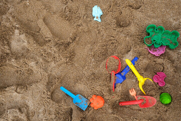 Fototapeta na wymiar Light brown tint grungy textured sand background with children's toys for digging. Copy space.Bright plastic children's toys in the sand. Concept of beach recreation for children. Top view. Space for