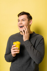 Fototapeta premium Positive man holding coffee to go on yellow background