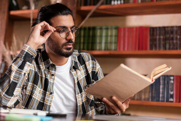 Indian Male Student Reading Book Learning Sitting In Library Indoors