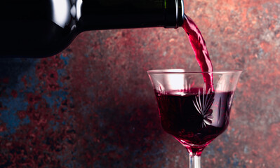Port wine or fortified red wine is poured from a bottle into a glass on a rusty brown background.