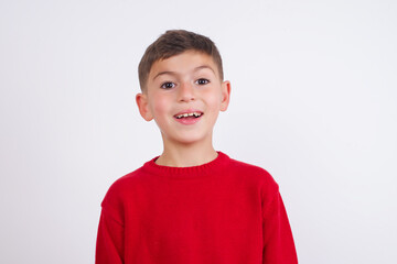 Surprised Little cute boy kid wearing red knitted sweater against white wall, shrugs shoulders,...