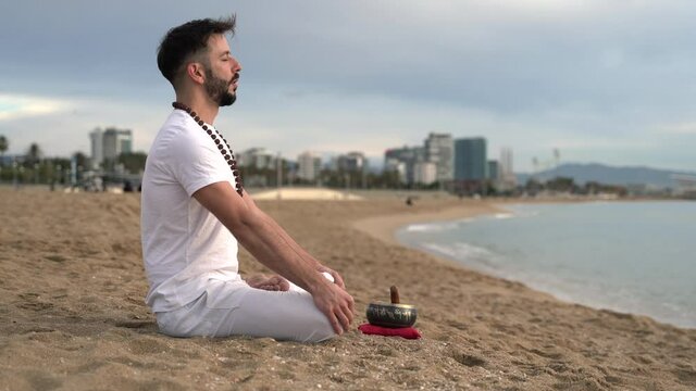 Young man meditating and singing om mantra in the beach 