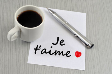 Je t'aime écrit sur un morceau de papier à côté d'une tasse de café