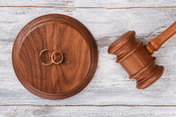 Gavel and wedding rings. Top view twp golden rings on wooden sounding block. White desk background.