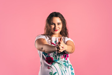 Happy plus size model doing gun gesture on pink background