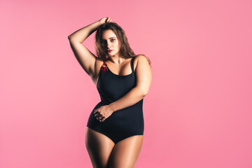 Fototapeta na wymiar Sexy plus size fashion model in black one-piece swimsuit, fat woman in lingerie on pink background