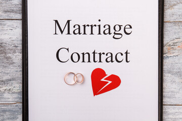 Marriage contract or divorce concept. Two golden rings and broken heart on a clipboard.